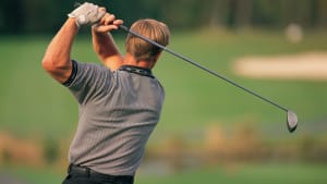 A person in a striped shirt swings a golf club on a lush green course, aiming for an eagle, which means scoring two strokes under par.